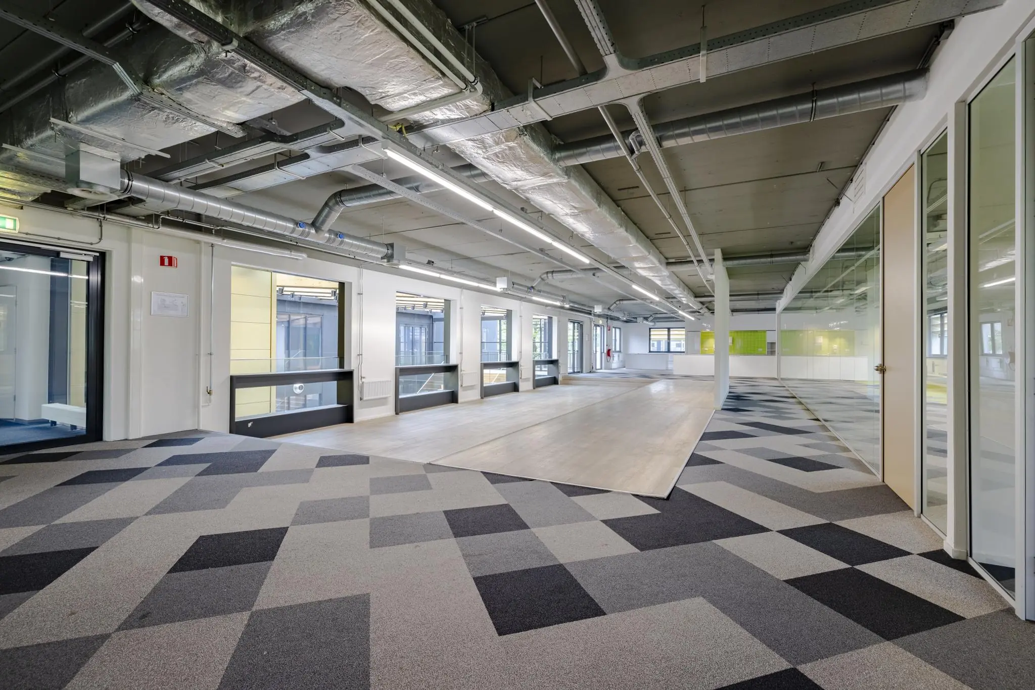 Moderne, lichte kantoorruimte aan de Laarderhoogtweg met geometrisch tapijt en zichtbare luchtkanalen aan het plafond.