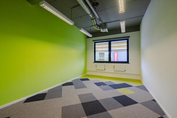 Lege kantoorruimte aan de Laarderhoogtweg met groene muur en kleurrijk tapijt.
