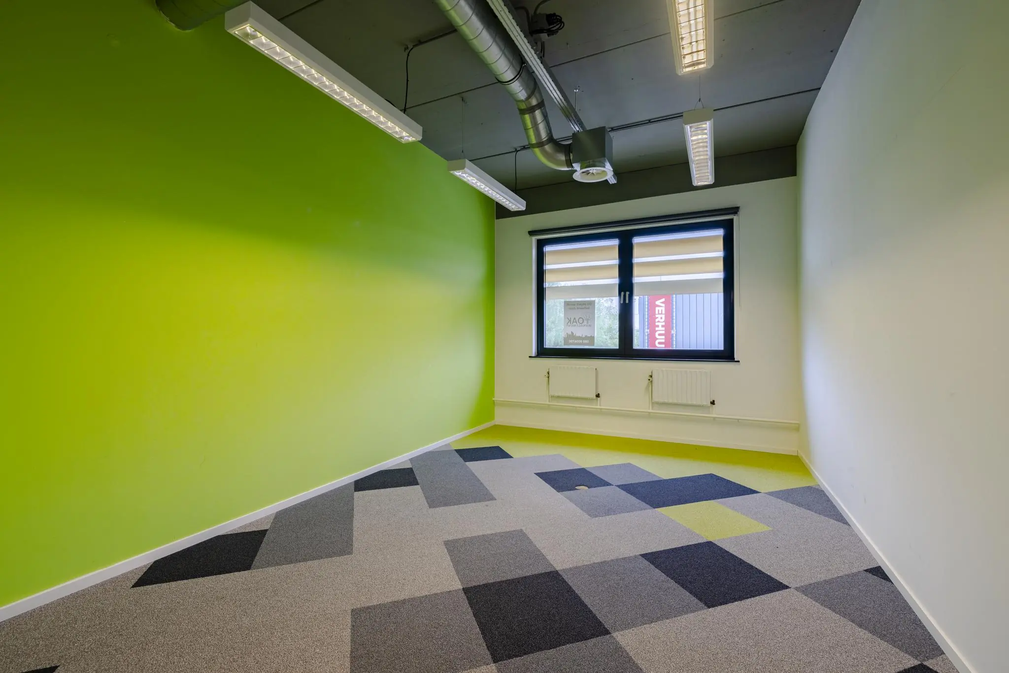 Lege kantoorruimte aan de Laarderhoogtweg met groene muur en kleurrijk tapijt.