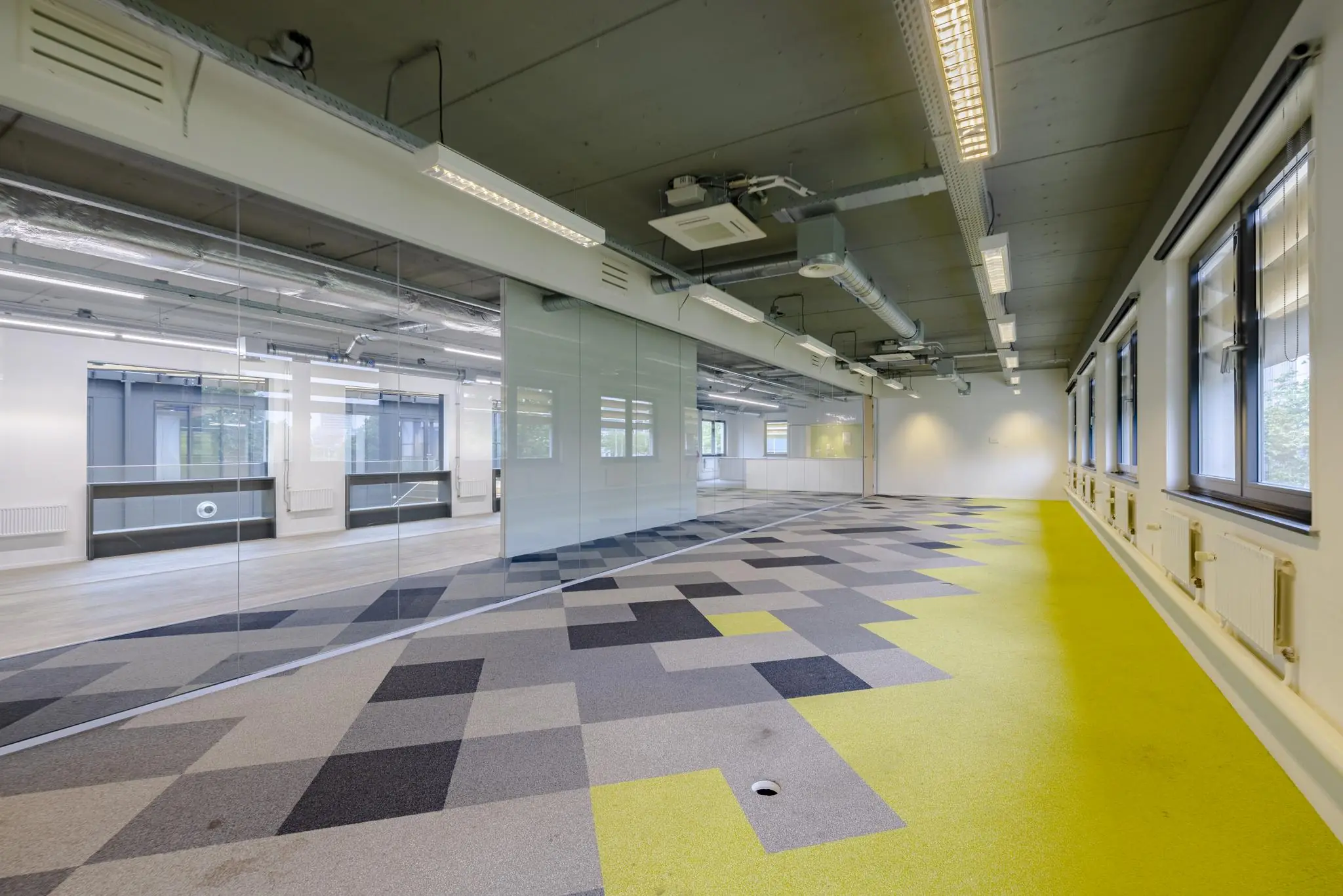Moderne, lege kantoorruimte aan de Laarderhoogtweg met glazen wanden, industrieel plafond en kleurrijk patroon op de vloerbedekking.
