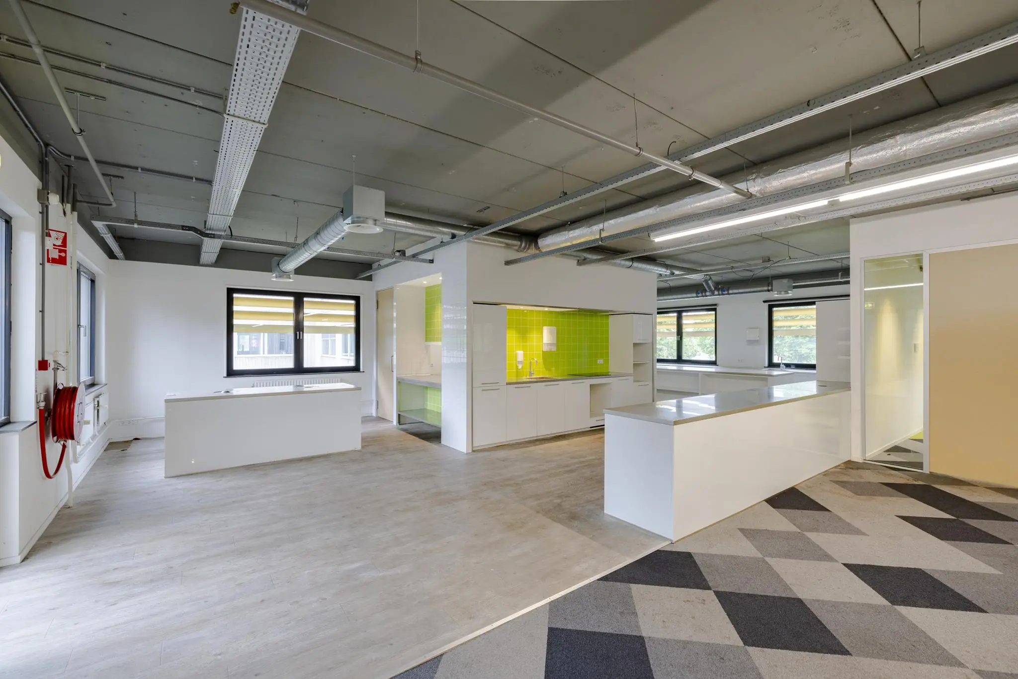 Moderne open kantoorruimte met een centrale kitchenette met felgroene tegels en witte kasten.