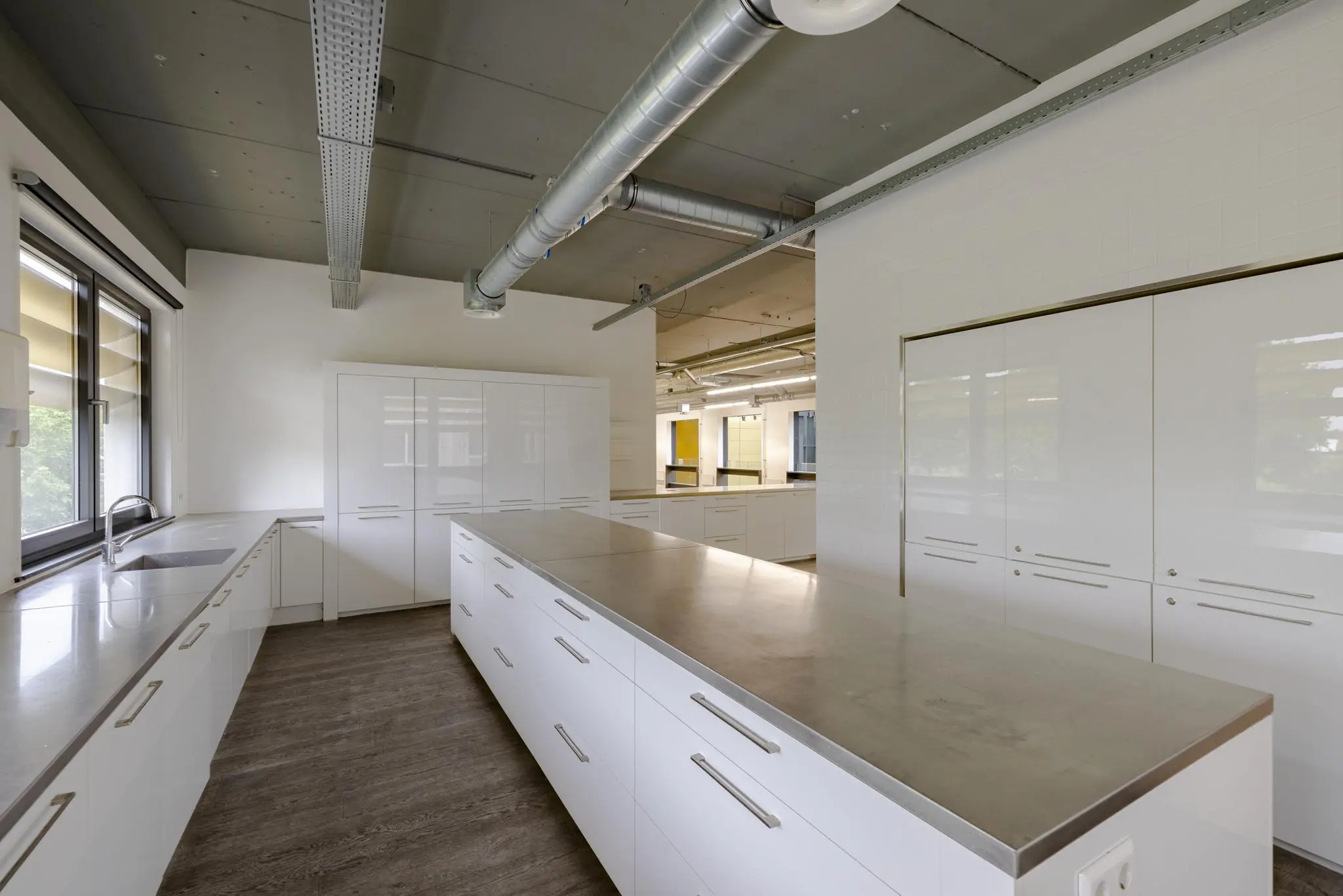 Moderne, ruime keuken met witte kasten, roestvrijstalen werkbladen en industriële plafonddetails aan de Laarderhoogtweg.