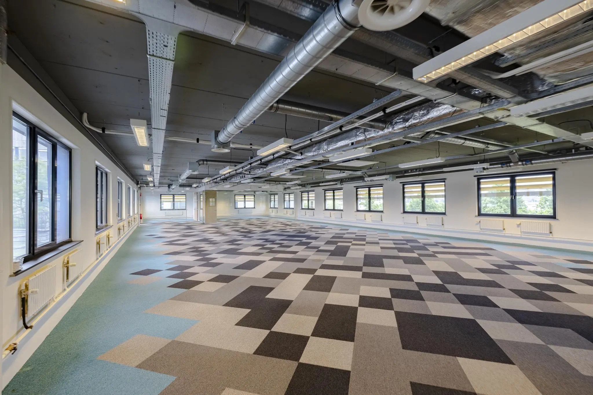 Modern, leeg kantoorpand aan de Laarderhoogtweg met geometrisch patroon op de vloer en zichtbare plafondinstallaties.