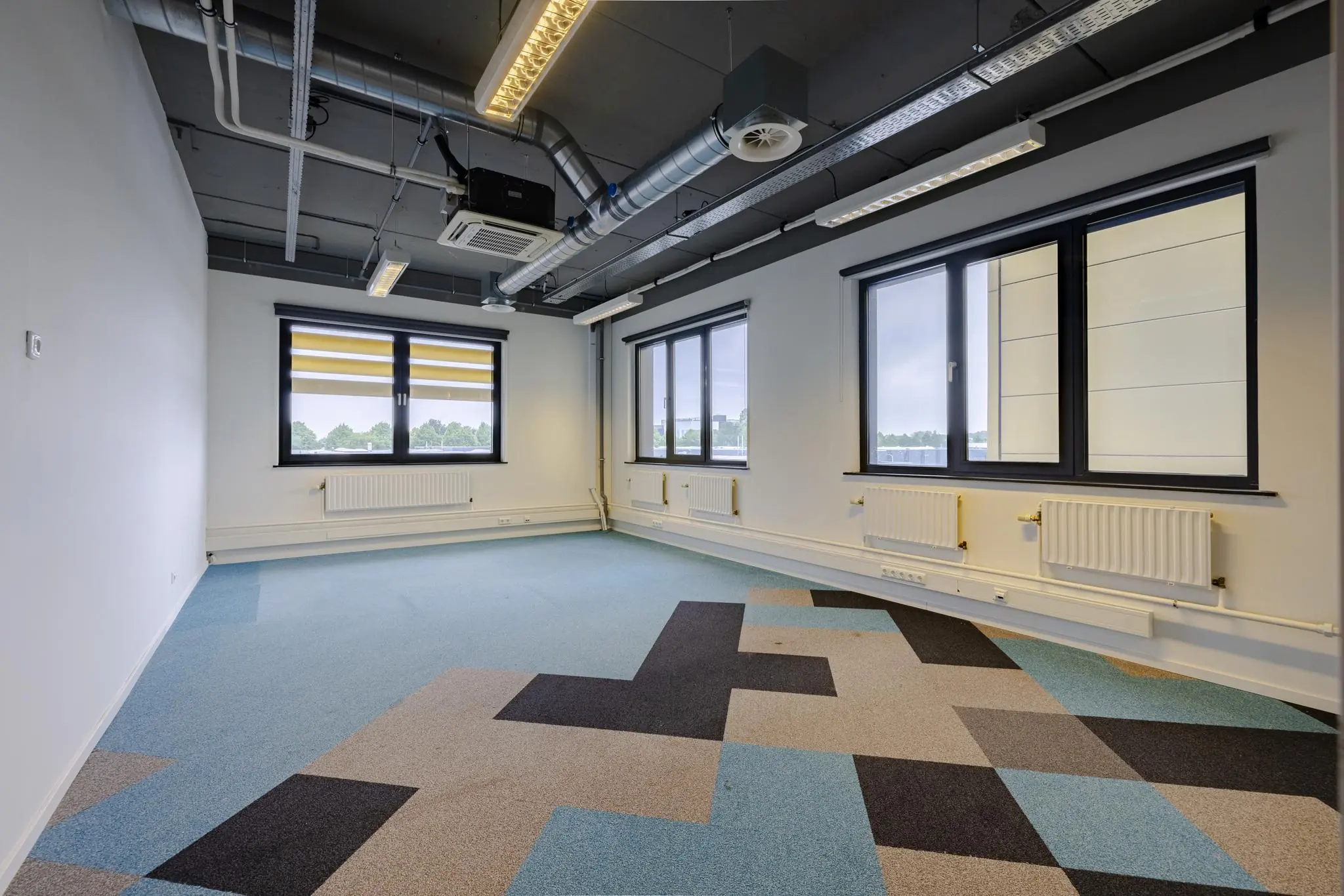 Lege kantoorruimte aan de Laarderhoogtweg met industrieel plafond en gekleurd tapijt.