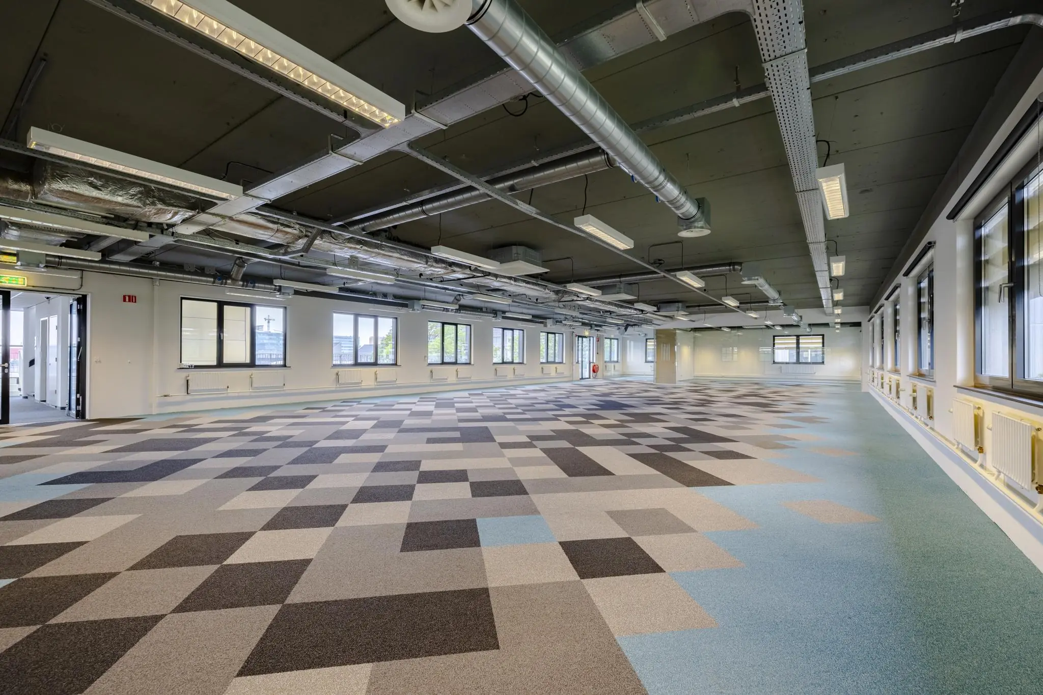 Leeg kantoorpand aan de Laarderhoogtweg met een modern industrieel plafond en vloerbedekking in een patroon van grijze en blauwe tegels.