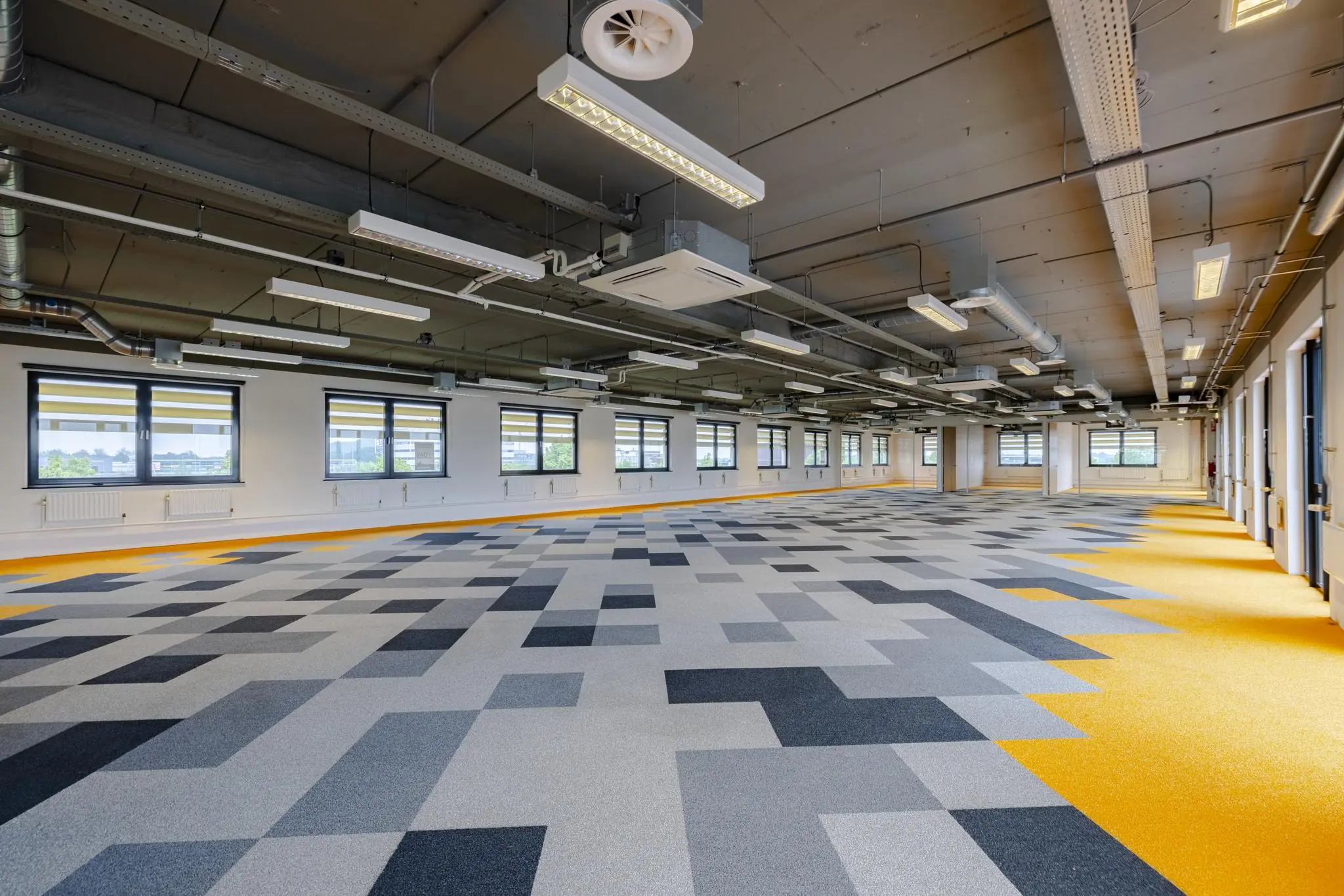 Ruime, moderne kantoorruimte aan de Laarderhoogtweg met opvallende vloerbedekking in grijs- en geeltinten en industriële plafonafwerking.