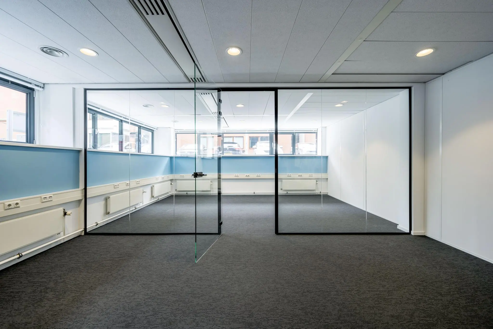 Modern kantoorinterieur met glazen vergaderruimte, blauwe lambrisering en grijze vloerbedekking aan de Stroombaan.