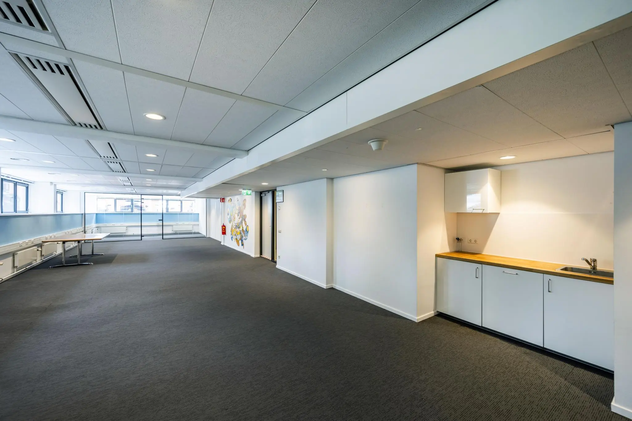 Kantoorruimte met een pantry, vergadertafels, grote ramen en een glazen wand in het Stroombaan-gebouw.
