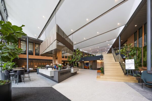 Moderne en open kantoorlobby aan de Jachthavenweg met een centraal koffiepunt, veel groen en een houten trap naar de bovenverdieping.