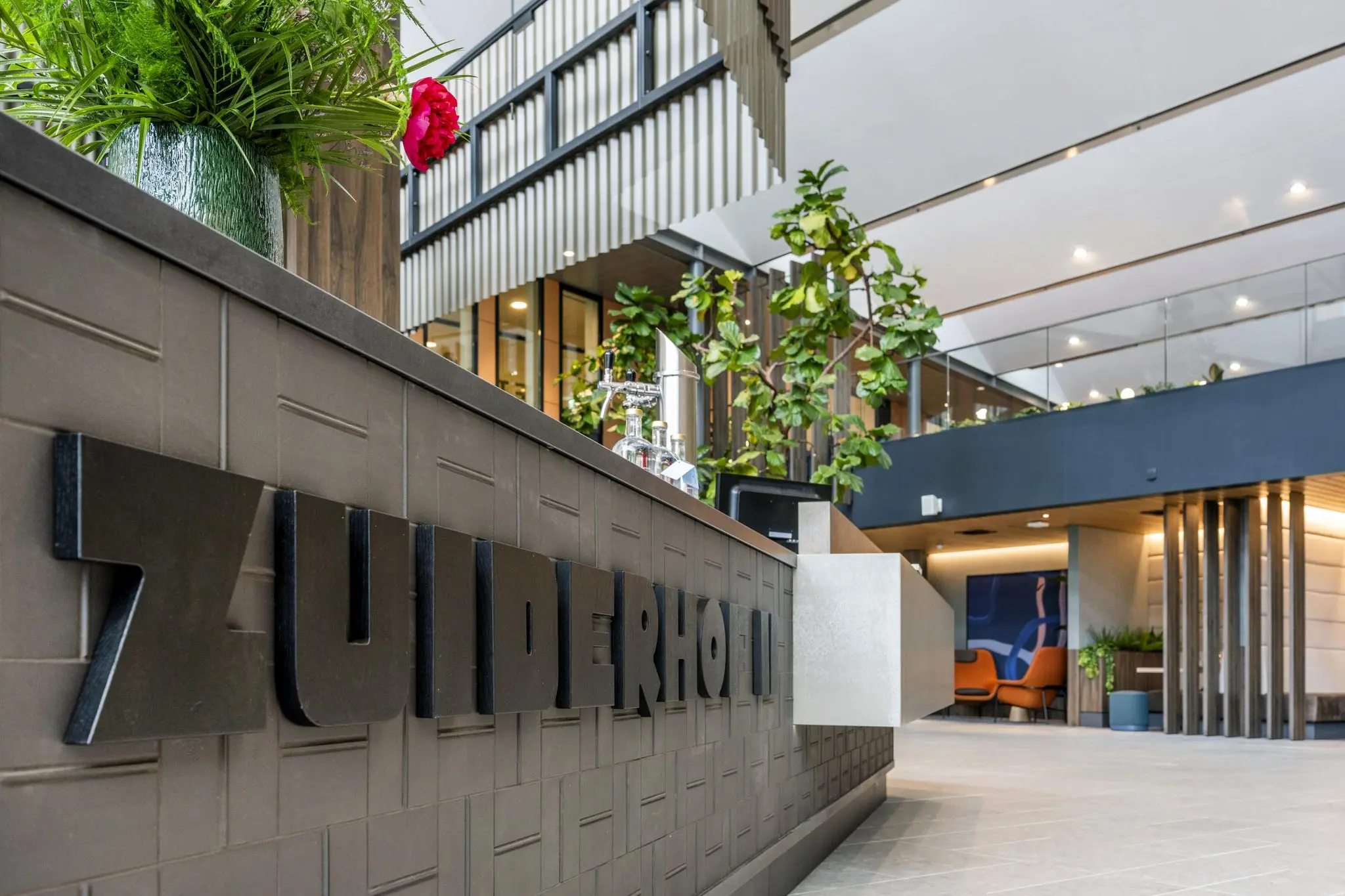 Moderne hotellobby van het Zuiderhof aan de Jachthavenweg met strakke inrichting, planten en een balie met logo.