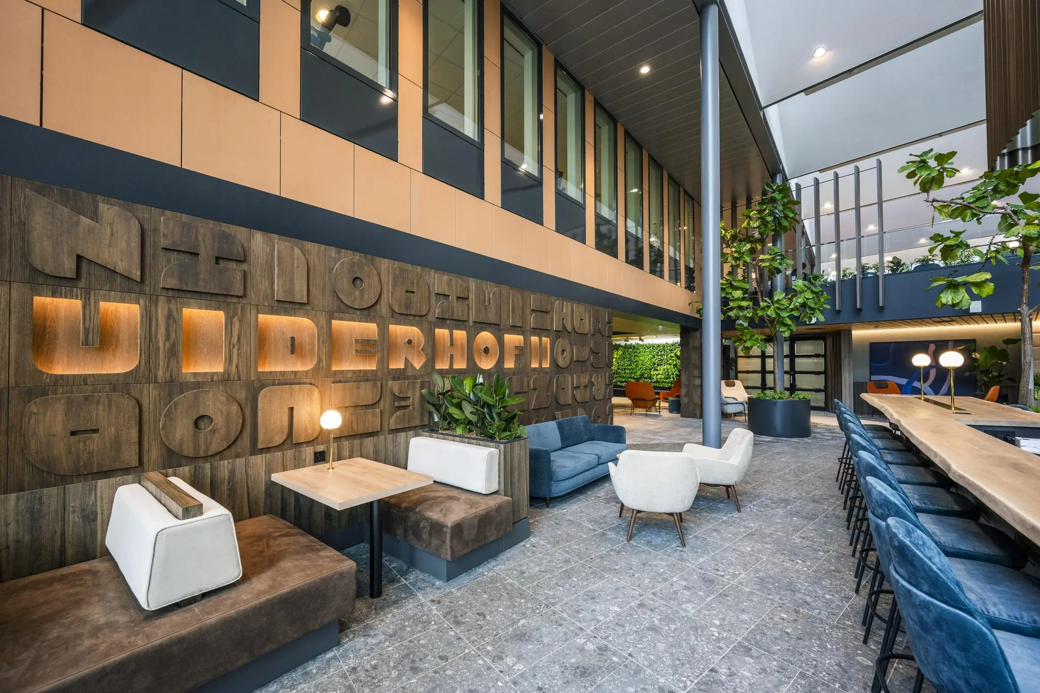 Moderne en ruime kantoorlobby aan de Jachthavenweg met zithoeken, planten en decoratieve houten wand met verlichte letters.