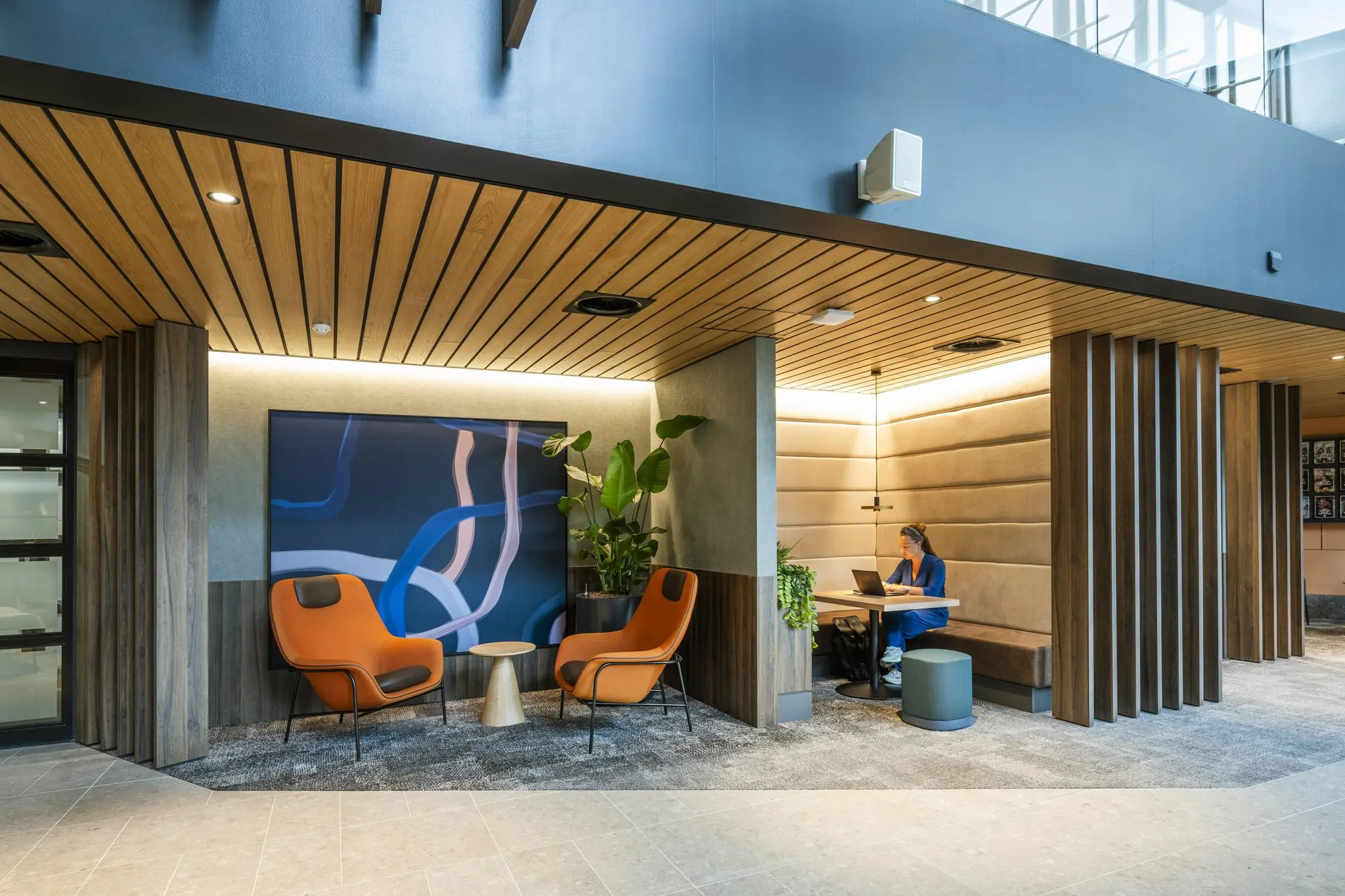 Moderne lounge- en werkruimte in een kantoorgebouw aan de Jachthavenweg, met zitgedeelte, kunst aan de muur en een persoon werkend op een laptop.