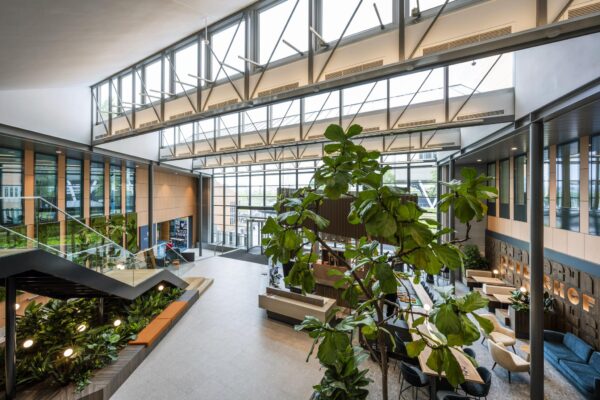Moderne, lichtovergoten lobby aan de Jachthavenweg met glazen gevel, grote planten en zithoeken.