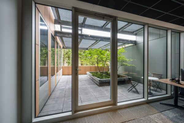 Doorkijk vanuit een kantoorruimte naar een groene binnentuin met zitgelegenheid aan de Jachthavenweg.