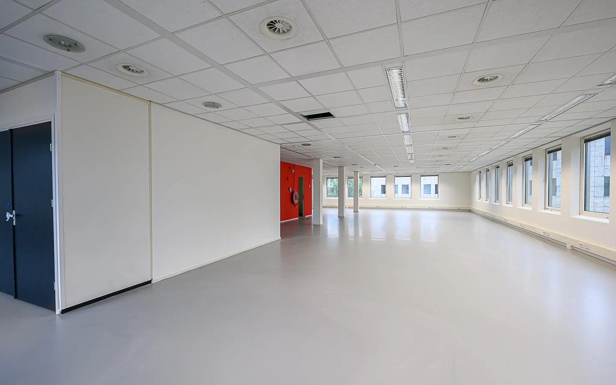Leeg kantoorpand aan de Rivium 1e Straat met witte wanden, systeemplafond en grote ramen.