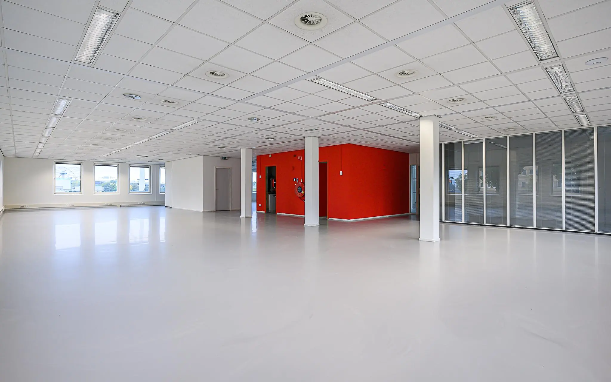 Lichte, lege kantoorruimte aan de Rivium 1e Straat met een opvallende rode wand en glazen scheidingswanden.