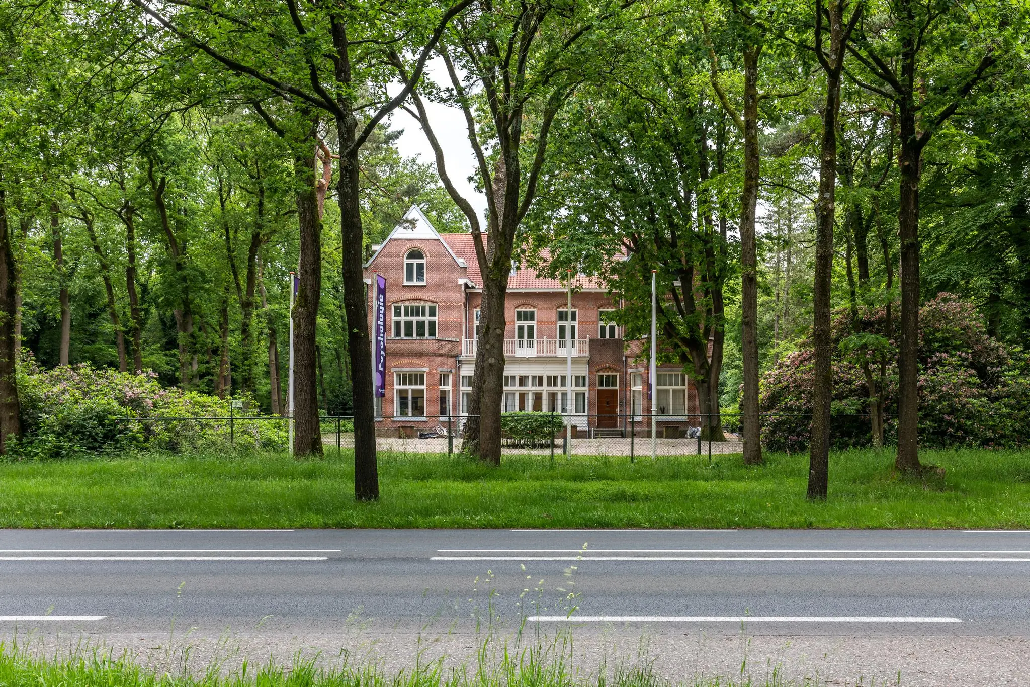 Vooraanzicht van een groot, rood bakstenen herenhuis aan de Amersfoortsestraat, omgeven door bomen en groen.
