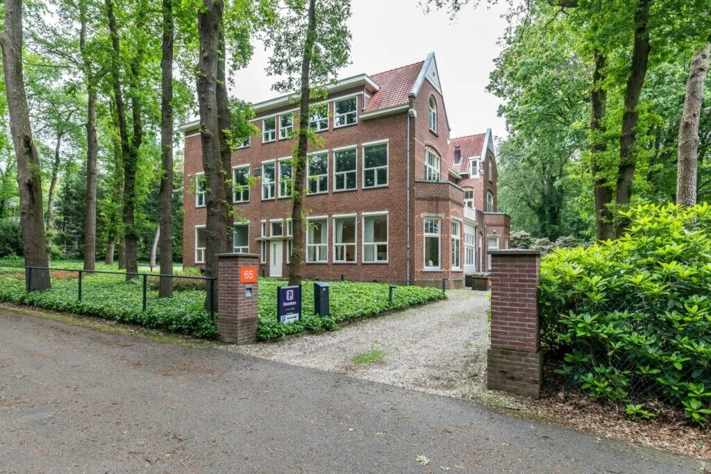 Groot herenhuis aan de Amersfoortsestraat 65 in een bosrijke omgeving met oprijlaan en parkeerbord.
