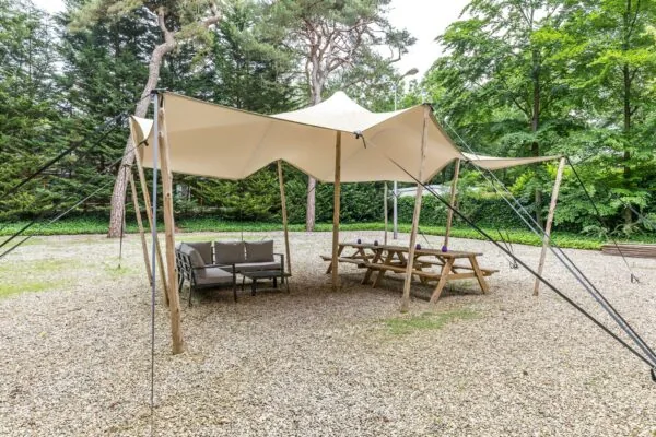 Overdekte buitentent met houten picknicktafels en loungeset op een grindterrein aan de Amersfoortsestraat.