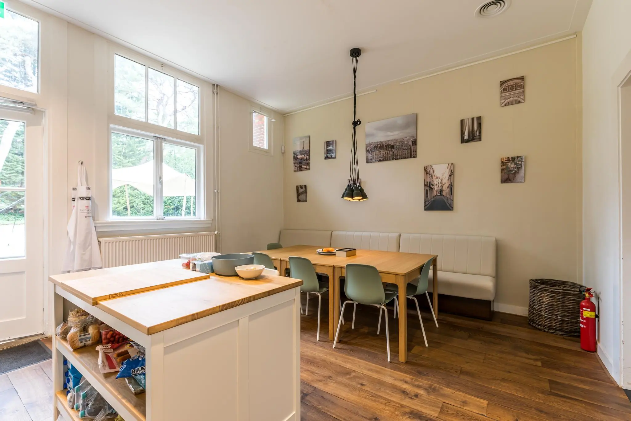 Moderne eetruimte met houten vloer, grote ramen, een keukeneiland en een zithoek met foto's aan de muur.