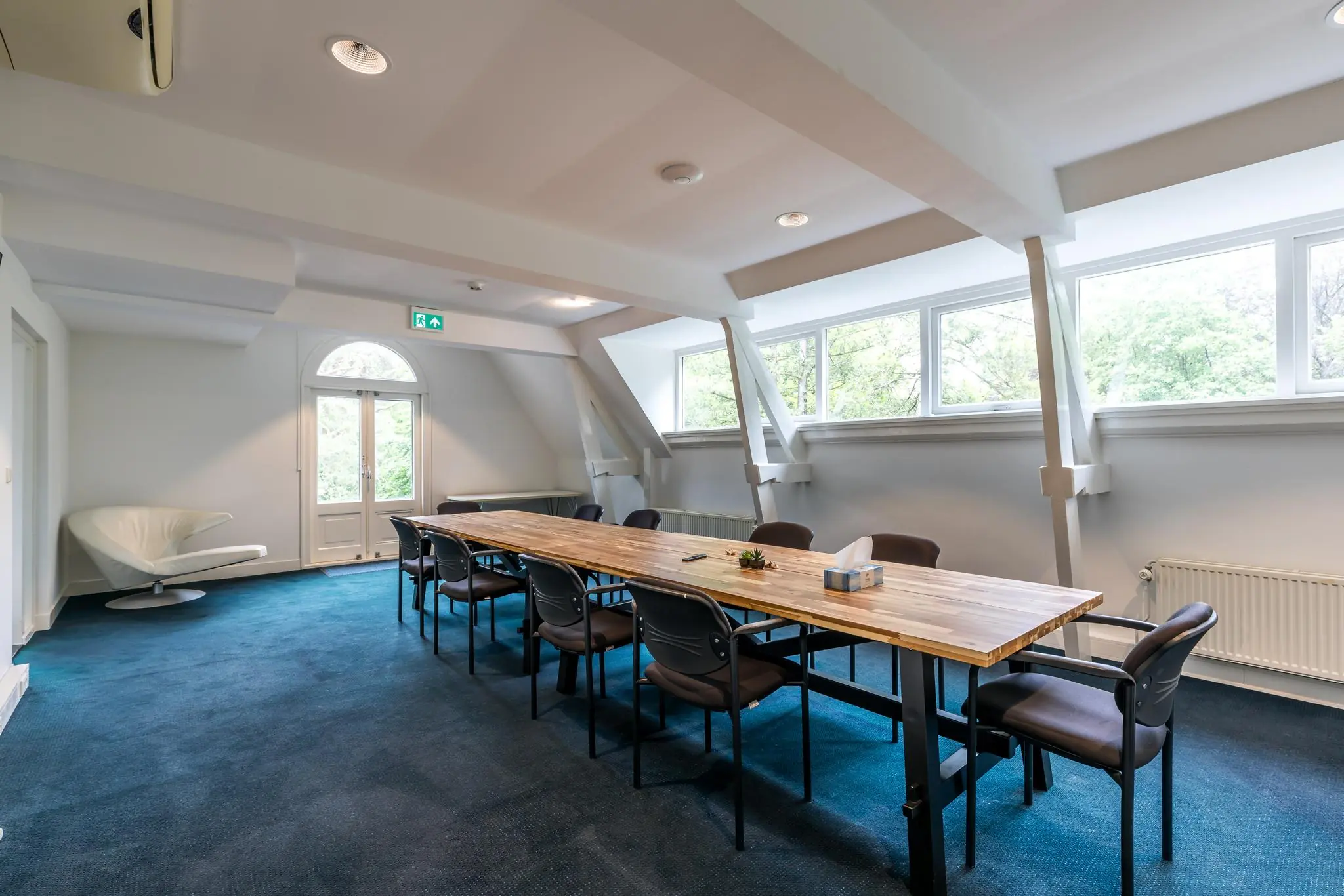 Vergaderruimte aan de Amersfoortsestraat met lange houten tafel, stoelen en grote ramen met uitzicht op bomen.