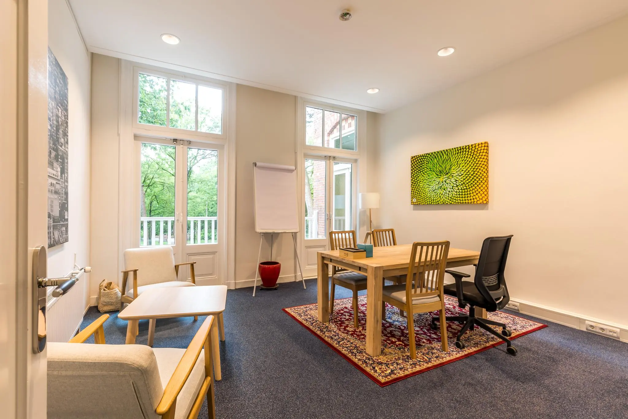 Vergaderruimte aan de Amersfoortsestraat met houten tafel, stoelen, flip-over en grote ramen met uitzicht op groen.