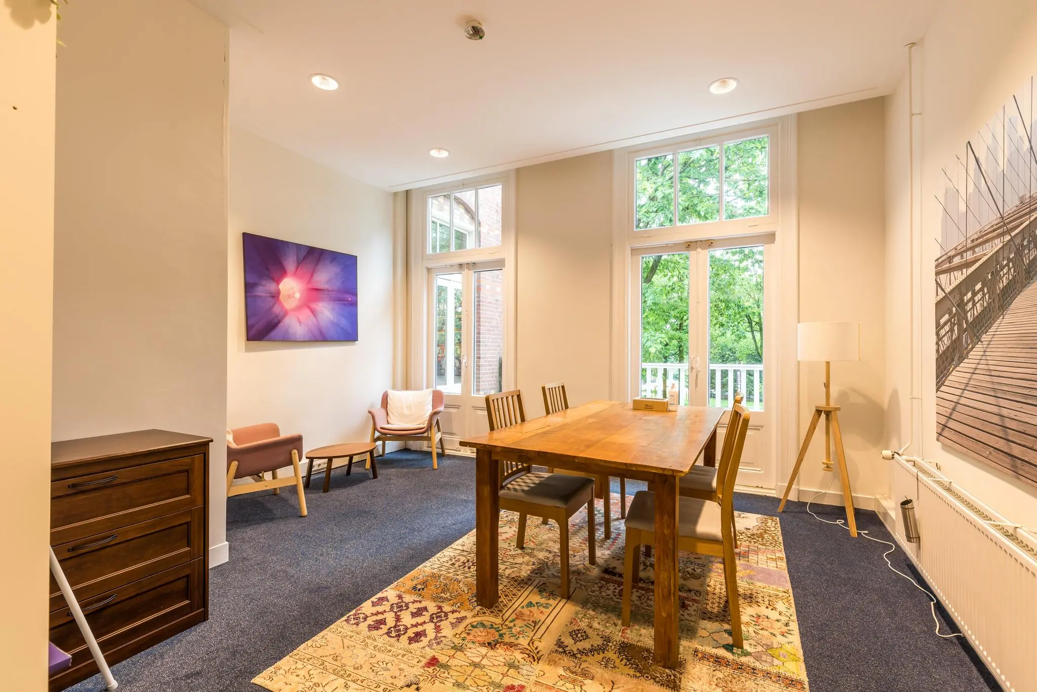 Lichte en sfeervolle vergaderruimte aan de Amersfoortsestraat met houten tafel, kunst aan de muur en uitzicht op groen.