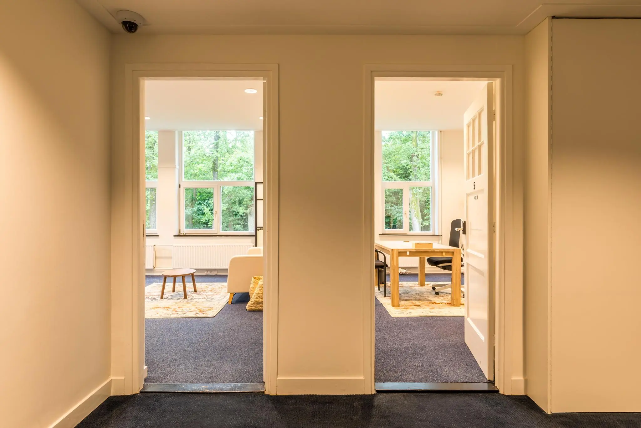 Twee aangrenzende kamers aan de Amersfoortsestraat met grote ramen, één ingericht als zithoek en de ander als kantoorruimte.