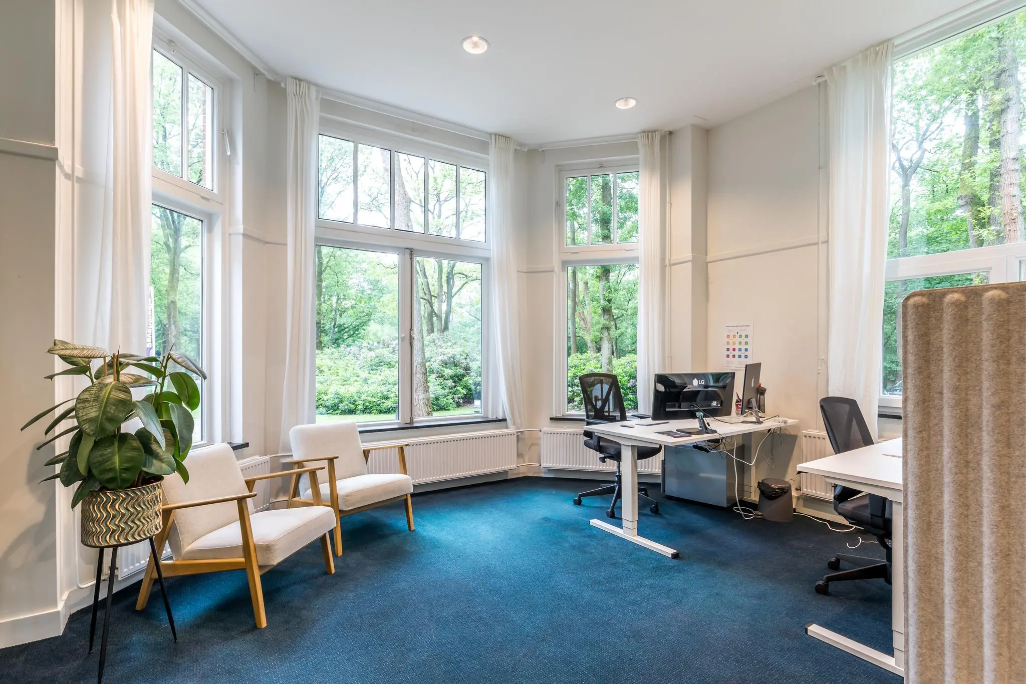 Modern ingericht kantoor aan de Amersfoortsestraat met grote ramen, bureaus en een zithoekje met stoelen en een plant.