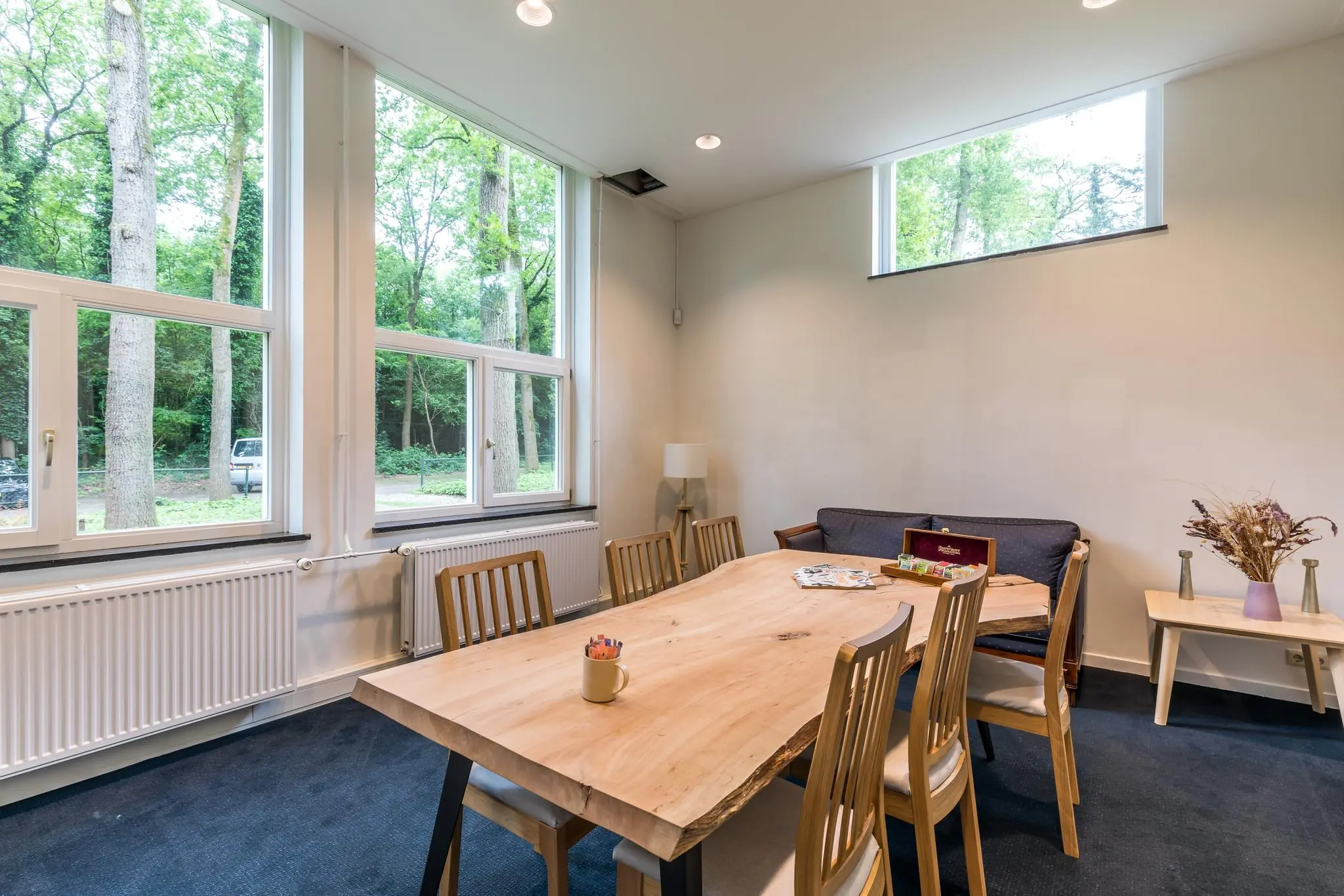 Vergaderruimte met houten tafel, zes stoelen en grote ramen met uitzicht op een bosrijke omgeving aan de Amersfoortsestraat.