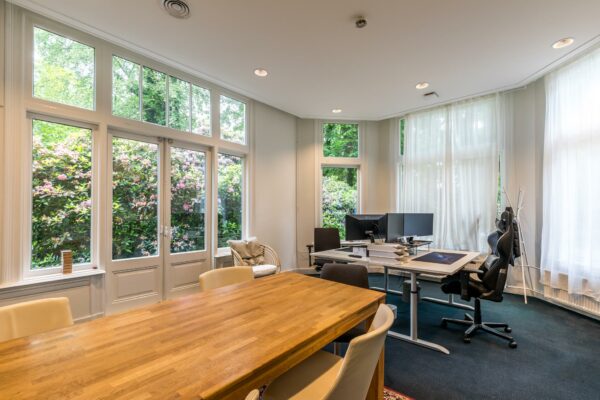 Licht en modern kantoor aan de Amersfoortsestraat met grote ramen, houten vergadertafel en werkplekken met computerschermen.