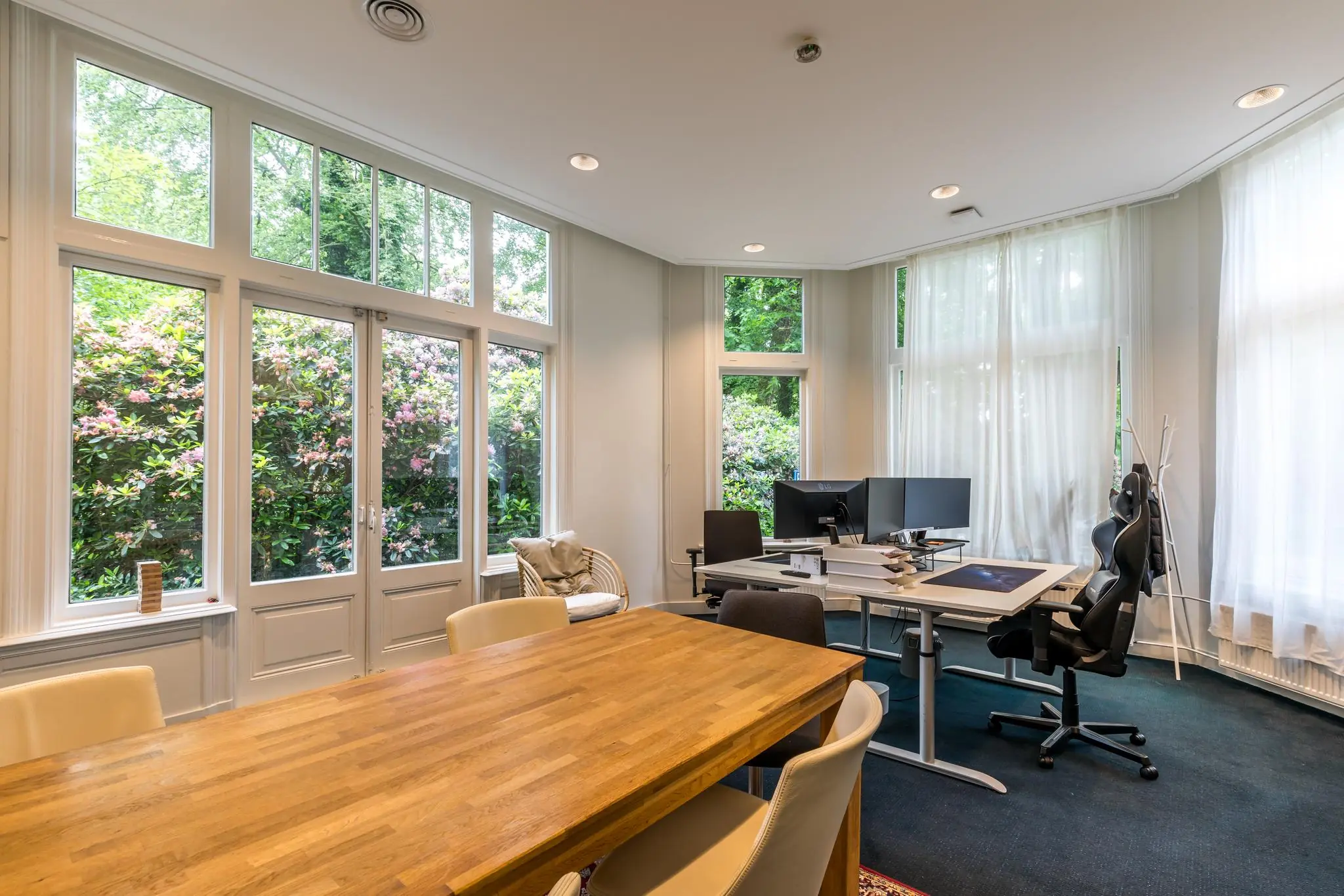 Licht en modern kantoor aan de Amersfoortsestraat met grote ramen, houten vergadertafel en werkplekken met computerschermen.