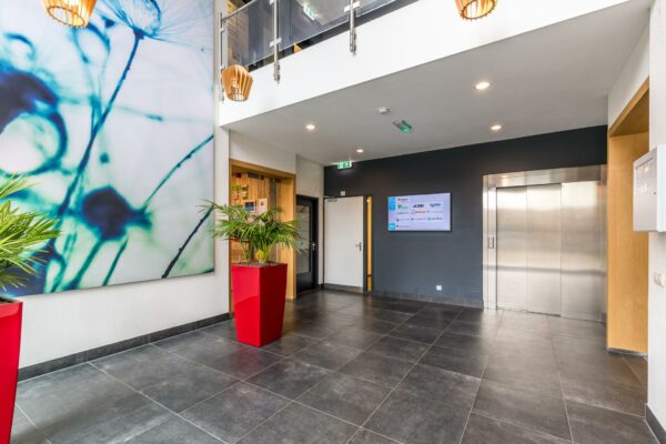 Moderne bedrijfslobby aan de Coltbaan met lift, planten in rode bakken en een groot kunstwerk aan de muur.