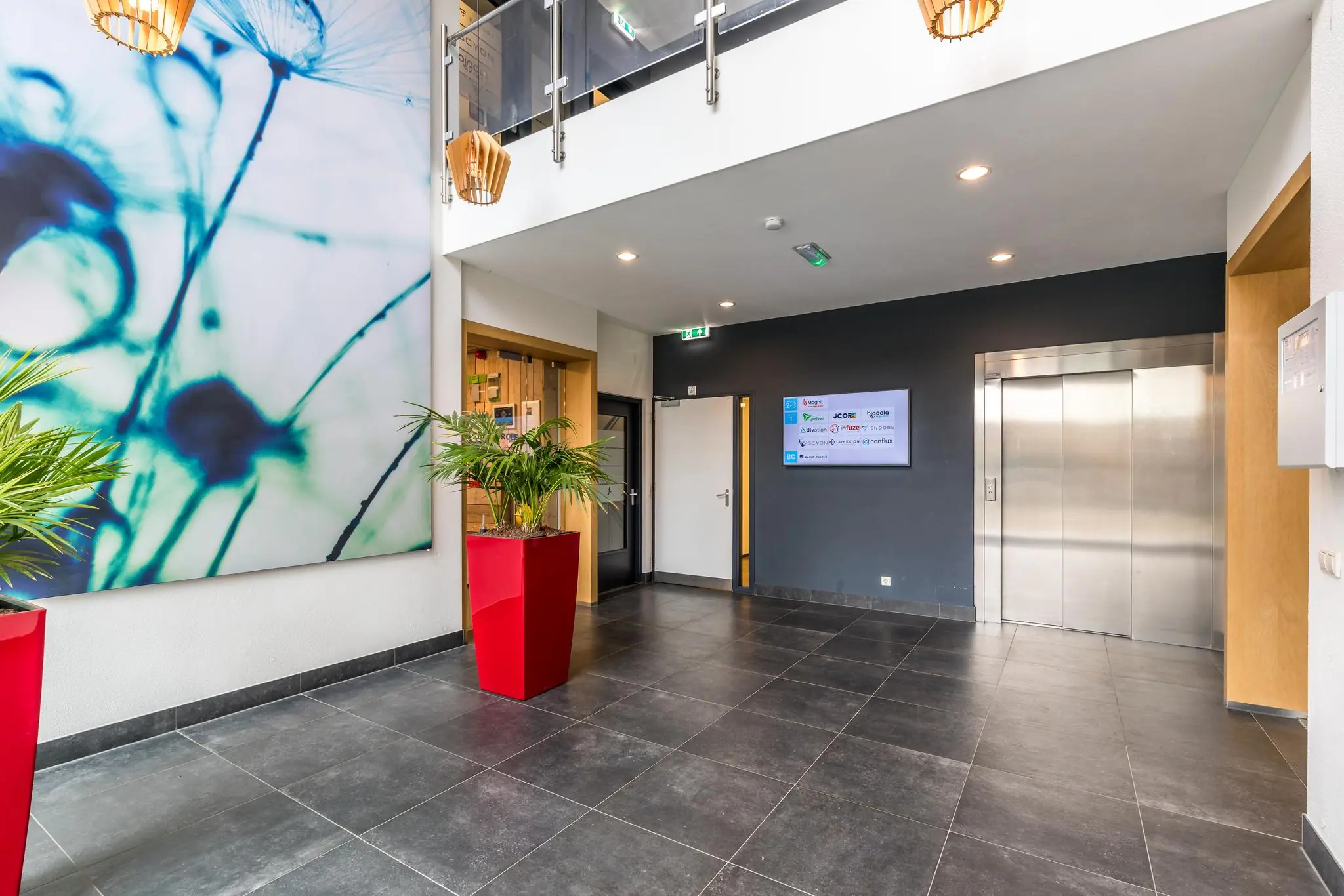 Moderne bedrijfslobby aan de Coltbaan met lift, planten in rode bakken en een groot kunstwerk aan de muur.