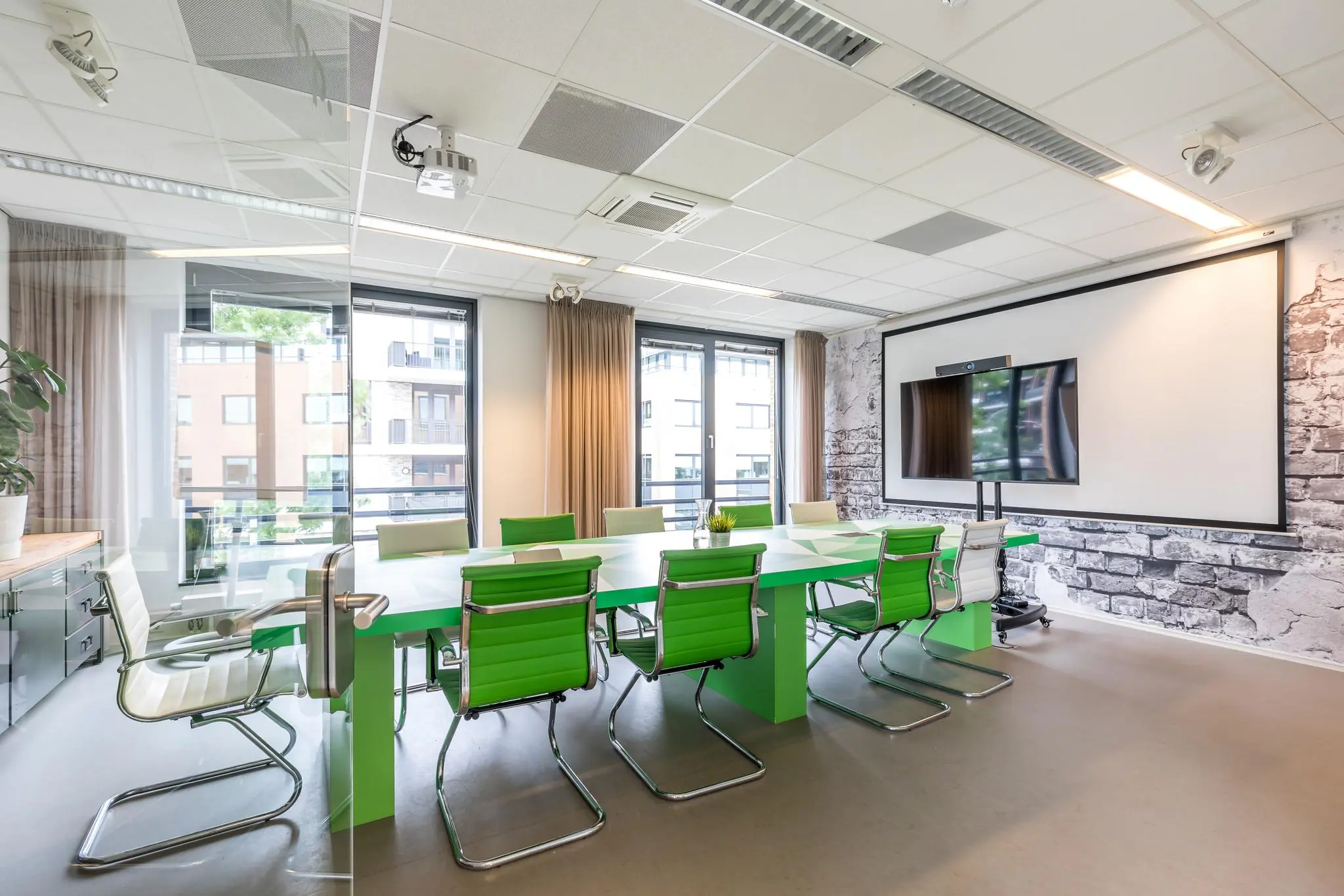 Moderne vergaderruimte aan de Coltbaan met groen-witte stoelen, glazen wand en presentatiescherm.