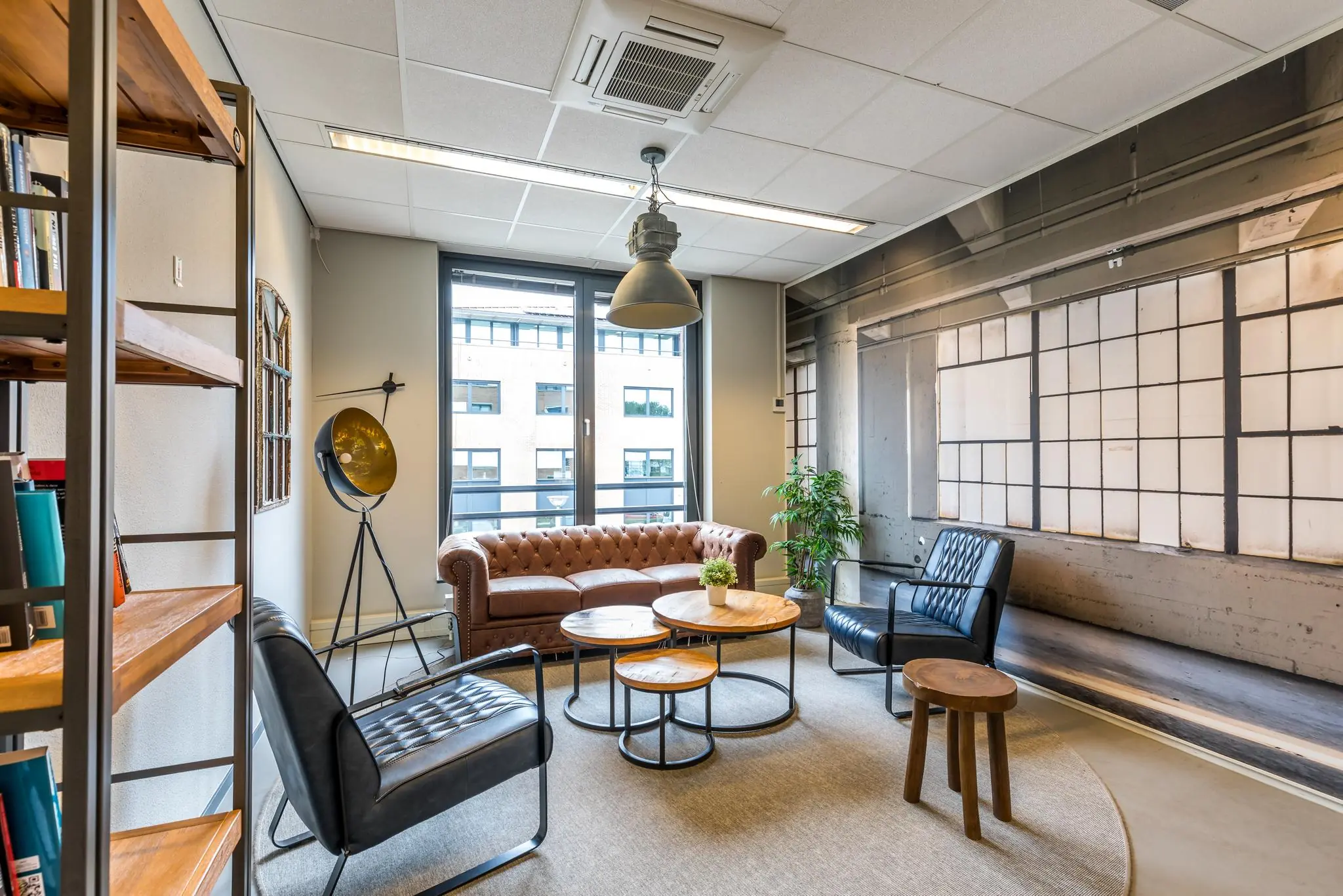 Stijlvol ingerichte loungehoek op Coltbaan met leren zitmeubels, ronde houten tafels en industriële accenten.
