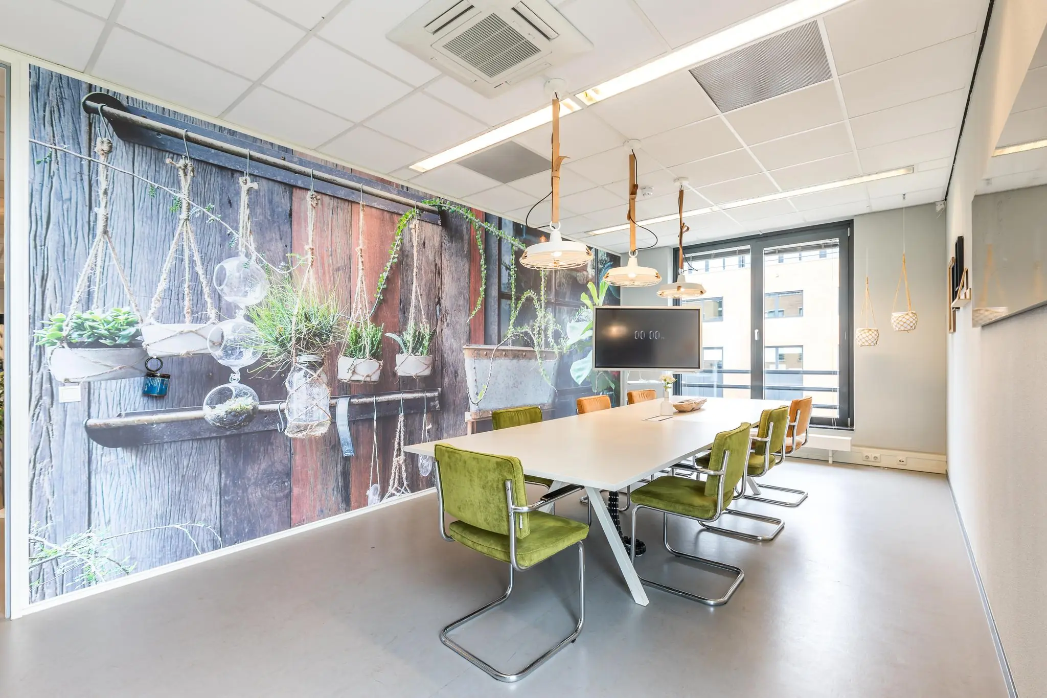 Vergaderruimte met groene stoelen, een grote tafel, hanglampen en een opvallende muurdecoratie met plantenprints aan de Coltbaan.