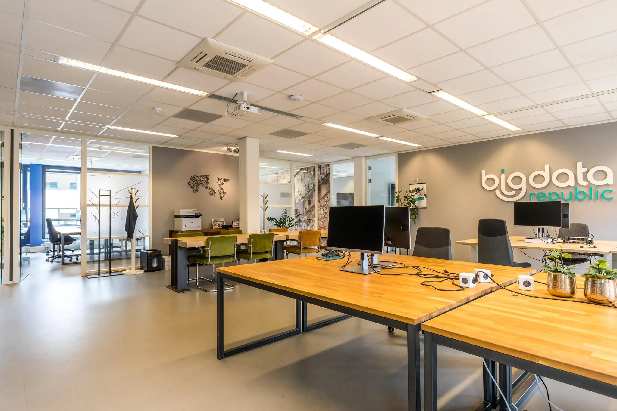 Moderne kantoorruimte van Big Data Republic met houten bureaus, computers en een minimalistisch interieur.