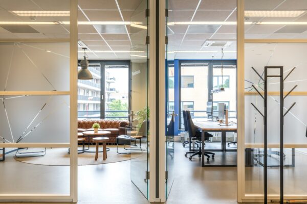 Moderne kantoorruimte aan de Coltbaan met een vergaderruimte links en werkplekken rechts, gescheiden door glazen deuren.