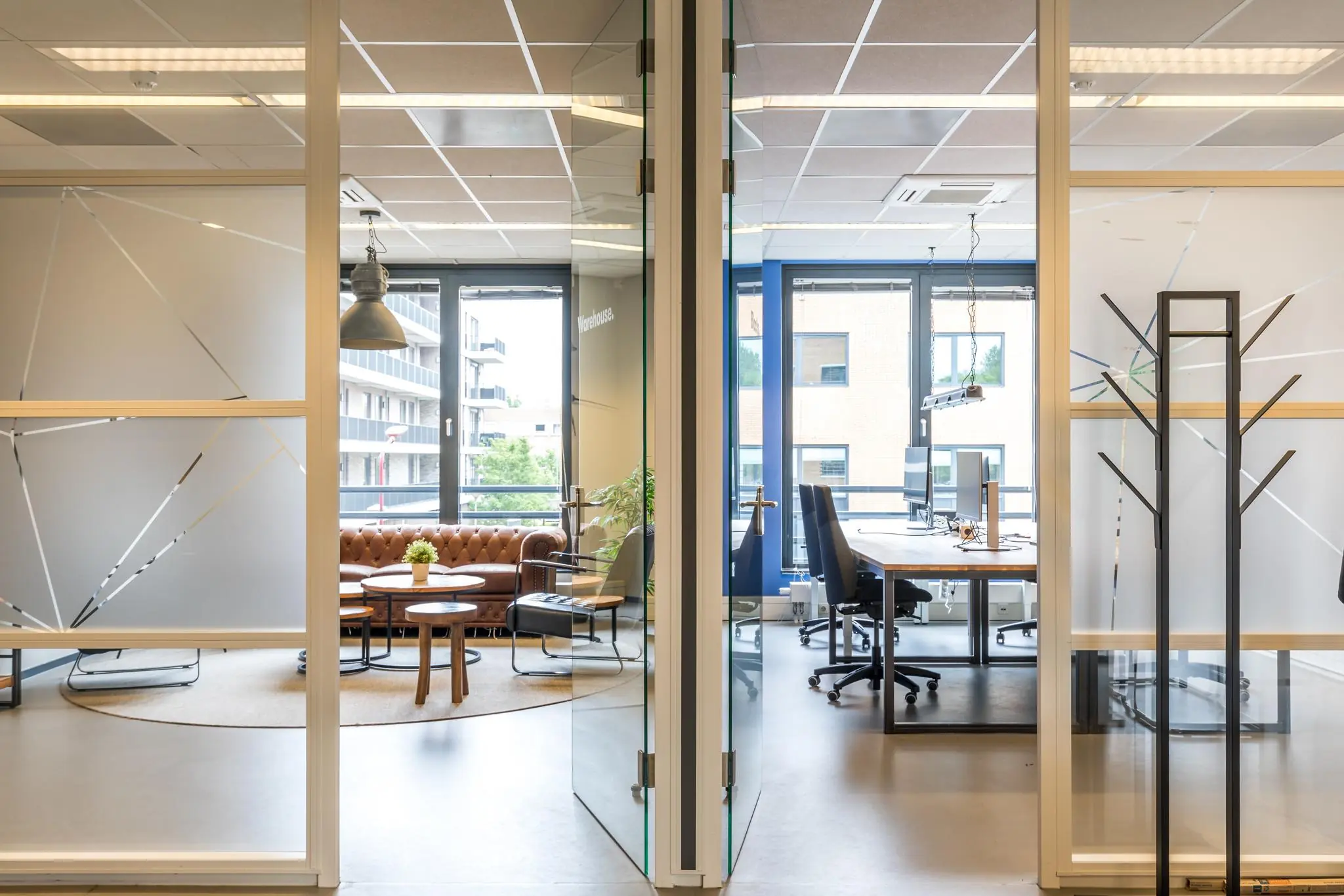 Moderne kantoorruimte aan de Coltbaan met een vergaderruimte links en werkplekken rechts, gescheiden door glazen deuren.