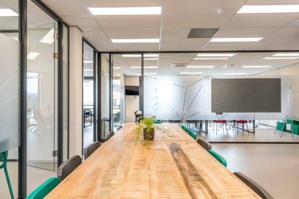 Moderne vergaderruimte met houten tafel, groene stoelen en glazen wanden in een kantoorpand aan de Coltbaan.