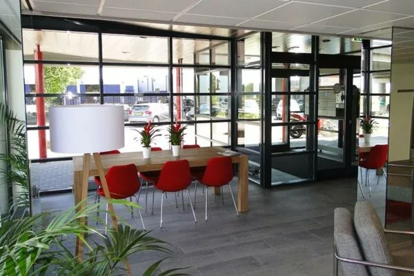 Moderne entree met glazen wanden, een houten tafel met rode stoelen en planten aan de Vanadiumweg.