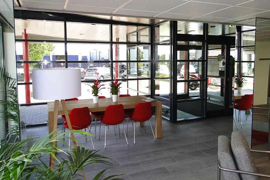 Moderne entree met glazen wanden, een houten tafel met rode stoelen en planten aan de Vanadiumweg.
