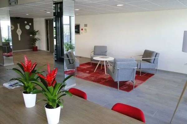 Moderne wachtruimte met grijze stoelen, een rood vloerkleed en kamerplanten aan de Vanadiumweg.
