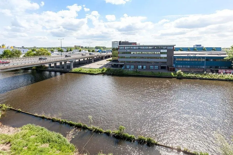 Kantoorgebouw aan de Vanadiumweg in Amersfoort gelegen langs een kanaal, met een brug en snelweg op de achtergrond.