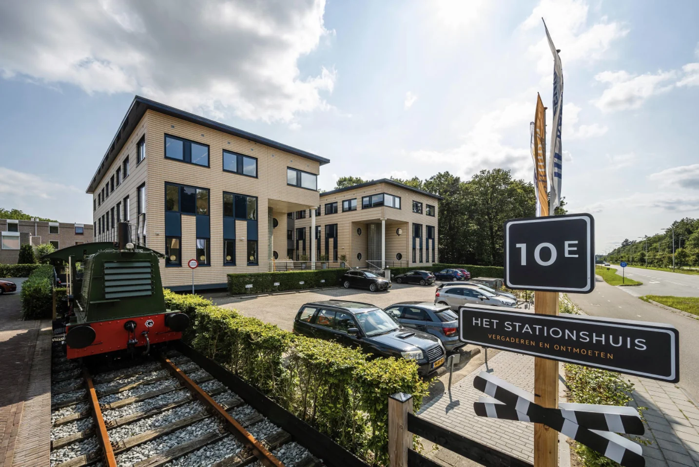 Modern kantoorgebouw aan de Amersfoortseweg met parkeerplaats, oud treinstel en een bord met de tekst "Het Stationshuis – Vergaderen en Ontmoeten".
