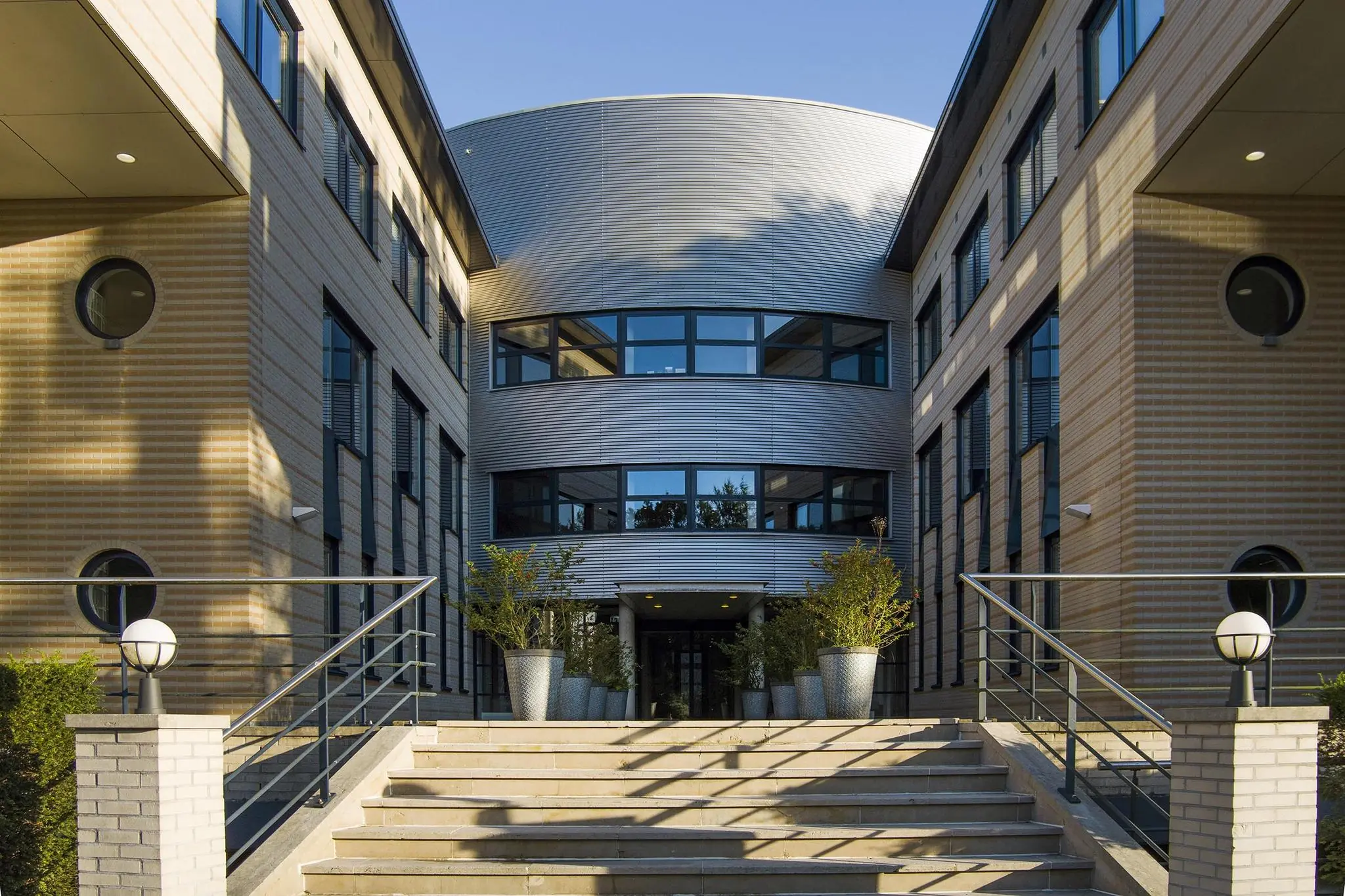 Ingang van een modern kantoorpand aan de Amersfoortseweg met trap, plantenbakken en symmetrische gevels.