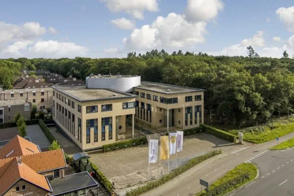 Luchtfoto van een modern kantoorpand aan de Amersfoortseweg, omringd door groen en gelegen aan een rotonde.