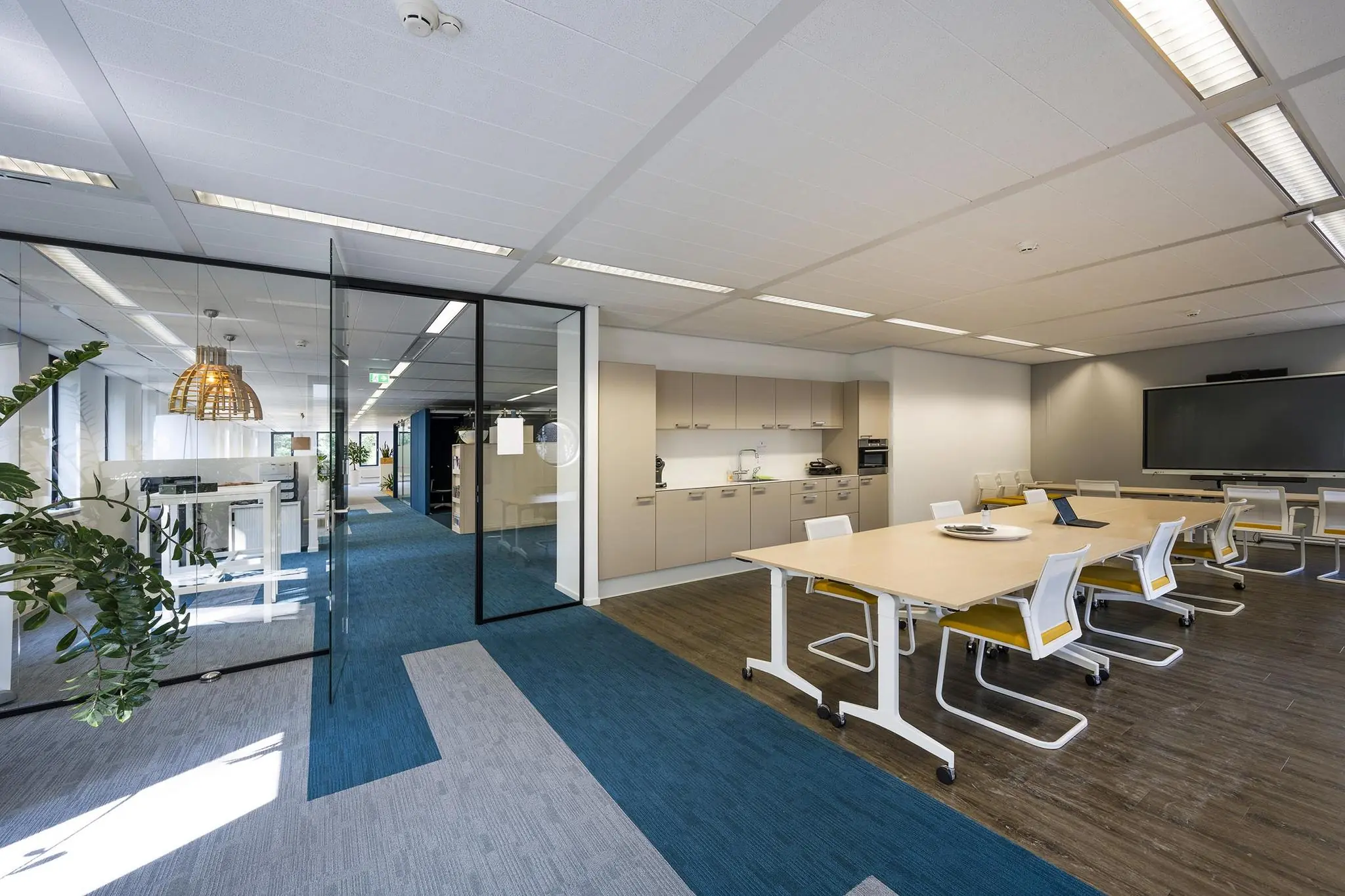 Moderne kantoorruimte aan de Amersfoortseweg met vergadertafels, open keuken en glazen wanden.