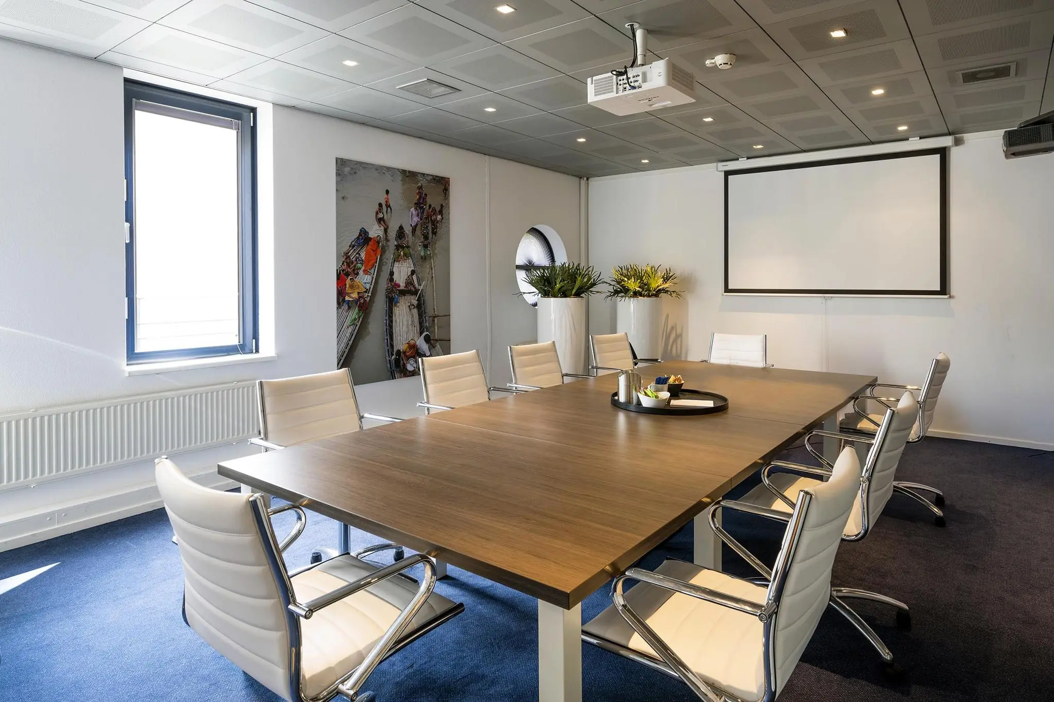 Moderne vergaderruimte aan de Amersfoortseweg met een lange tafel, witte stoelen, projectiescherm en decoratieve planten.